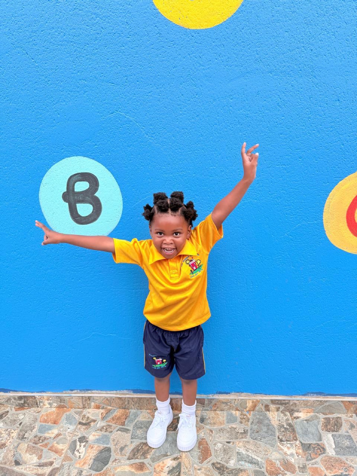 A Busy Bees girl in uniform with her arms up at the painted letter wall