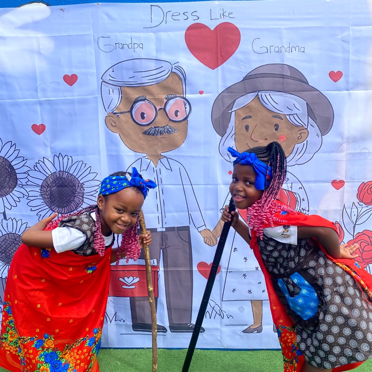 Two girls dressed as grandmothers in traditional attire at the Grandparents' Day banner